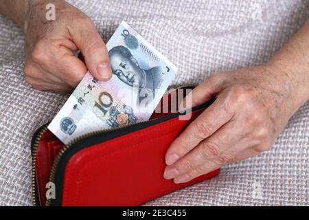 Ältere Frau nimmt chinesische Yuan-Notiz aus ihrer Brieftasche. Konzept der Pensionszahlungen in China, Einsparungen im Ruhestand, Rentner mit Geld Stockfoto