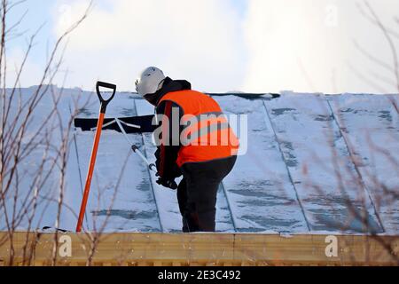 Arbeiter, der Schnee auf dem Dach eines Gebäudes entfernt. Schneeräumung, Kletterdach im Winter reinigen Stockfoto