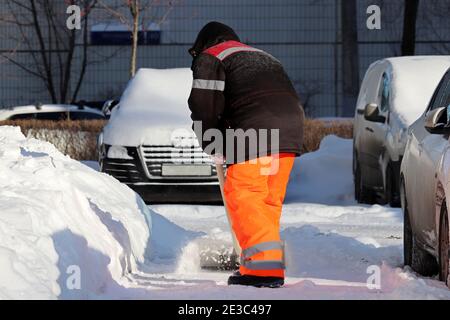 Schneeräumung in der Winterstadt, Straßenreinigung. Arbeiter in der Uniform mit der Schaufel auf dem Parkplatz Stockfoto