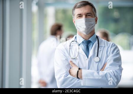 Heiter reifer Arzt in Gesichtsmaske posiert bei Kamera, Gesundheit und Medizin. Stockfoto