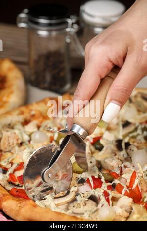 Frauenhand schneidet die Pizza mit einem Pizzabesser. Hausgemachte Pizza. Lieferung nach Hause. Stockfoto