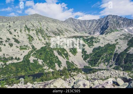 Bergtal mit Steinkamm und Bäumen am Horizont. Reisen Sie im Sommer durch wilde Felsen. Berglandschaft gegen blauen Himmel an sonnigen Tagen Stockfoto