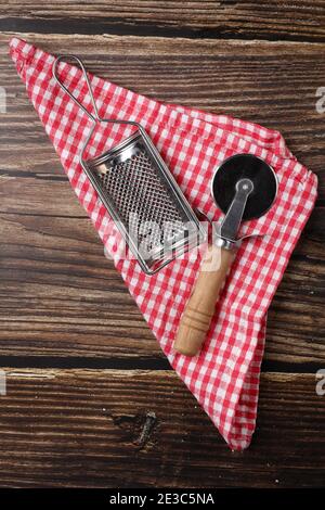Pizzabesser und Käsereibe auf einer weißen und roten Serviette auf einem Holztisch. Pizza kochen. Stockfoto