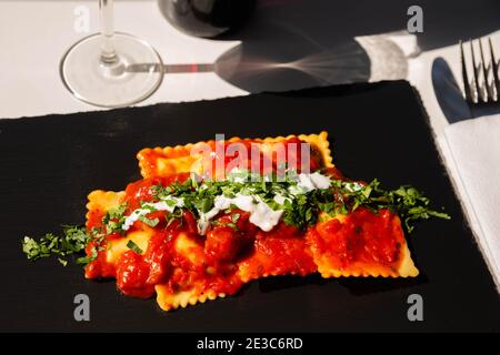 Vier mit Käse gefüllte Ravioli in Tomaten- und Basilikumsoße auf dem schwarzen Steinteller, einem berühmten Gericht aus der französischen Stadt Nizza Stockfoto