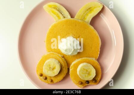 Kreatives Essen für ein Kind, Pfannkuchen mit Banane, Schokolade und Schlagsahne in Hasenform, lustiges Essen Stockfoto