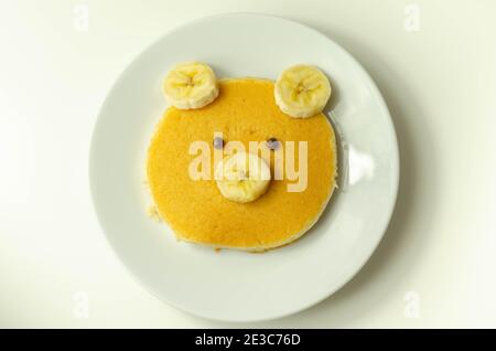 Kreative Mahlzeit für ein Kind, Pfannkuchen mit Banane und Schokolade in einem Gesicht kleine Bärenform, lustige Lebensmittel Stockfoto