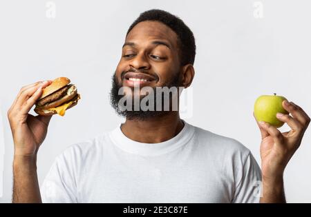 Black Guy Holding Burger Und Apple Choosing Food, Weißer Hintergrund Stockfoto