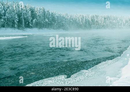 Frostiger Nebel über dem Winterfluss mit Schnee und Wald am Ufer. Erstes Eis am See an kalten Tagen. Stockfoto