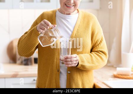 Nahaufnahme einer nicht erkennbaren Großmutter, die Wasser in das Glas gießt Stockfoto