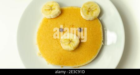 Kreative Mahlzeit für ein Kind, Pfannkuchen mit Banane und Schokolade in einem Gesicht kleine Bärenform, lustige Lebensmittel Stockfoto