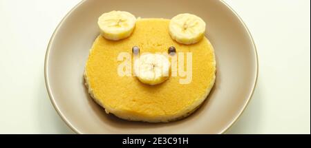 Kreative Mahlzeit für ein Kind, Pfannkuchen mit Banane und Schokolade in einem Gesicht kleine Bärenform, lustige Lebensmittel Stockfoto