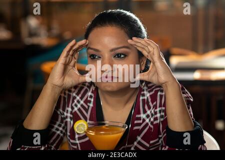 Eine hübsche Frau mit einem besorgten Gesichtsausdruck schaut weg von der Kamera, während sie Saft in einem Restaurant trinkt. Stockfoto