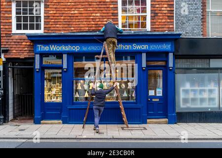 Eine Frau hält EINE Leiter für einen älteren Mann, der Immobilien baut, Lewes, East Sussex, Großbritannien. Stockfoto