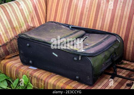 Stornierte Reisepläne Konzept während COVID 19, Coronavirus, Lockdown Reiseverbot. Schimmeliger Koffer draußen auf verfallendem Sofa entsorgt Stockfoto