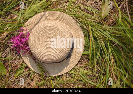 Strohhut mit einem kleinen Bouquet von lila Wildblumen auf dem grünen Gras. Stockfoto