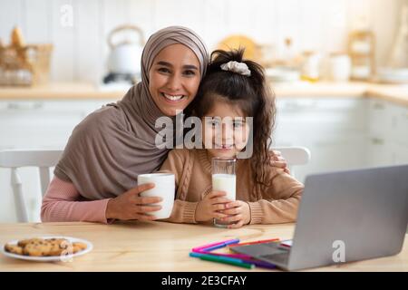 Glückliche Muslimische Mutter Und Kleine Tochter Mit Snacks Und Getränken In Der Küche Stockfoto