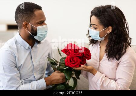 Schwarzes Paar in medizinischen Gesichtsmasken mit Datum, halten Rosen Stockfoto