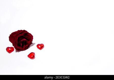 Das Konzept des Valentinstag. Die Rose Knospe ruht auf einem weißen Hintergrund. In der Nähe liegen kleine Herzen, selektiver Hintergrund, Kopierraum Stockfoto