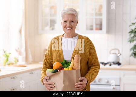 Glückliche reife Frau mit einem Papierbeutel voller Lebensmittel Stockfoto