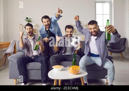 Begeisterte Freunde sitzen auf dem Sofa, beobachten Fußballspiel und unterstützen Lieblings-Team Stockfoto