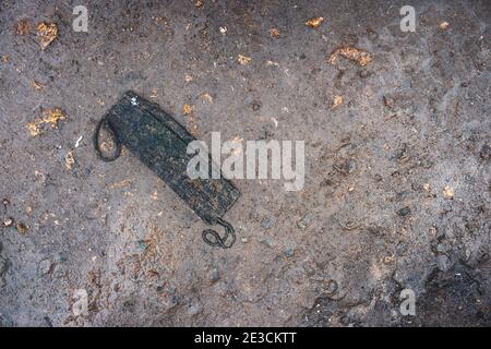 Gebrauchte zertrampelte schmutzige Stoff Gesichtsmaske liegt auf schlammigem Boden. Öffentliche Räume werden mit ausrangierten Schutzausrüstungen überflutet. Stockfoto