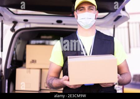 Liefermann Mitarbeiter in gelber Kappe und T-Shirt einheitliche Gesichtsmaske halten leere Karton-Box. Coronavirus und Kaufkonzept. Stockfoto