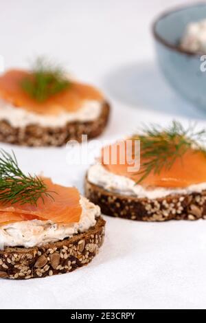 Drei Scheiben Proteinbrot mit Frischkäse und geräuchertem Lachs auf weißem Hintergrund, flachgelegt, appetitlich, Stockfoto