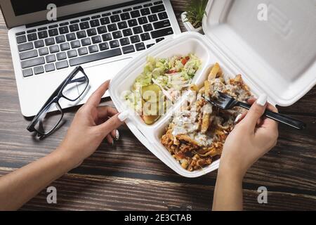 Lebensmittelbehälter auf Holztisch neben Laptop. Schnelle Lieferung von Lebensmitteln zu Hause. Essen Business Lunch zu Hause. Arbeiten Sie von zu Hause aus. Remote-Arbeit. Stockfoto