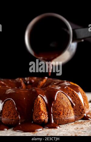 Geschmolzener heißer Schokoladenpudding wird von einem metallenen Kaffeekanne auf einen Schokoladenkuchen als Sahnehäubchen gegossen. Es fließt nach unten und macht braune Pfütze Stockfoto