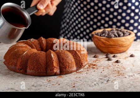 Ein Koch ist dabei, geschmolzene Schokolade auf einen runden Kuchen frisch aus dem Ofen zu gießen. Sie hält einen Krug aus Metall, in dem sich die geschmolzene Vereisung befindet. Der Stockfoto