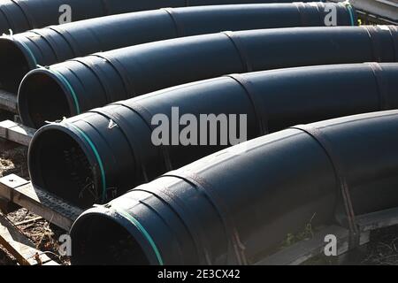 Schwarze Vergasungsrohre mit großem Durchmesser liegen an einem Sommertag in einer Reihe in einem offenen Lager auf der Straße. Stockfoto