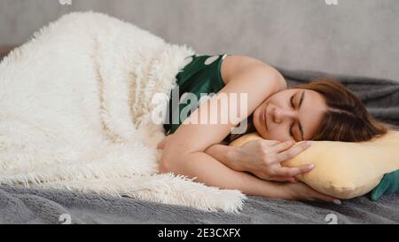 Schöne junge Mädchen in einem grünen Nachthemd schläft auf einem Gelbes Kissen auf einem Sofa unter einer weißen Decke Stockfoto