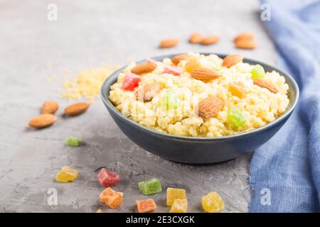 Hirsebrei mit kandierten Früchten und Mandeln in blauer Keramikschale auf grauem Betongrund und blauem Leinentextilien. Seitenansicht, Nahaufnahme, auswählen Stockfoto