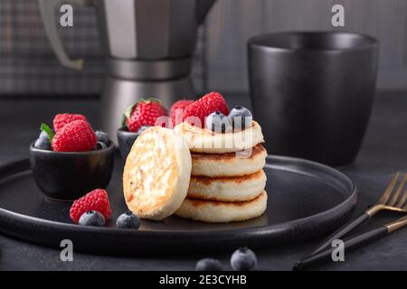 Hüttenkäse-Pfannkuchen mit frischen Beeren auf dunkler Keramikplatte. Syrniki - Bild Stockfoto