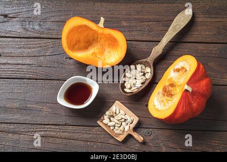 Kürbiskernöl in einer weißen Schüssel, frische Herbstbumkins und Kürbiskerne in Holzlöffeln und auf einem dunklen Holztisch, Draufsicht Stockfoto