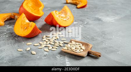 Scheiben von frischen Herbst-Pumkins und Kürbiskerne in einem Holzlöffel auf grauem Hintergrund mit Kopie spce Stockfoto