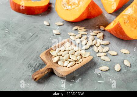 Pumkin Samen in einem Holzlöffel und Scheiben von frischen Herbstpuppen auf grauem Hintergrund Stockfoto