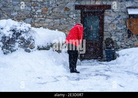 Mann mit Schneeschaufel reinigt Gehwege im Winter in der Nähe des Hauses. Winterzeit, Schneefall. Frankreich Europa. Unscharfer Fokushintergrund Stockfoto