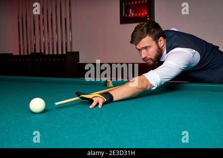 Mann, der Arm auf Billardtisch hält, Snooker-Spiel spielt oder sich darauf vorbereitet, Poolbälle zu schießen. Sportspiel Snooker Billard Stockfoto