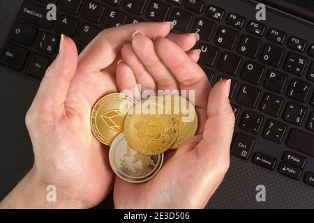 Frau mit goldfarbenen Kryptowährungsmünzen in den Händen Schwarze Laptop-Tastatur Stockfoto