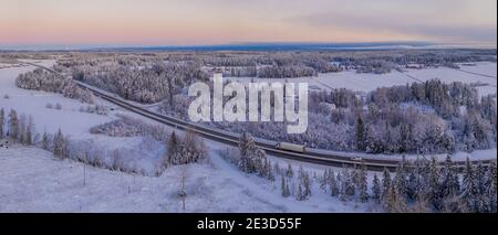 Spektakuläre Winter Luftaufnahme der Europäischen Route E4 in der Nähe von Umea Stadt. Landschaftlich gefrorener skandinavischer Kiefernwald, der von viel Schnee bedeckt ist. Stockfoto