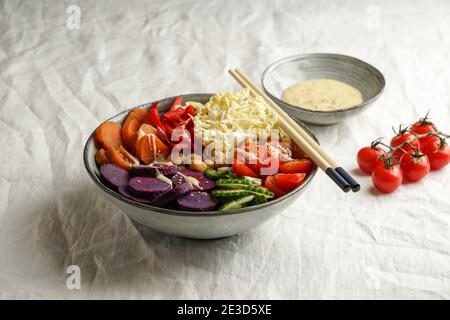 budha Schüssel mit violetten Batata, Paprika, Kohl, Süßkartoffeln, Kichererbsen, Gurken auf der weißen Leinentischdecke Stockfoto