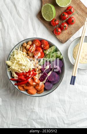 budha Schüssel mit violetten Batata, Paprika, Kohl, Süßkartoffeln, Kichererbsen, Gurken auf der weißen Leinentischdecke Stockfoto
