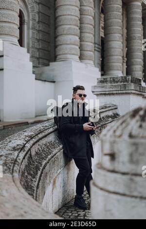 Junge gutaussehende männliche Fotograf hält professionelle Kamera, während in der Stadt stehen. Reisekonzept Stockfoto