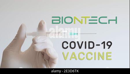 Hand mit Handschuh hält die Spritze neben dem BioNTech-Logo, einem der Unternehmen, das einen Covid-19 (Coronavirus)-Impfstoff entwickelt. Wien, Österreich - 18. Januar 2 Stockfoto