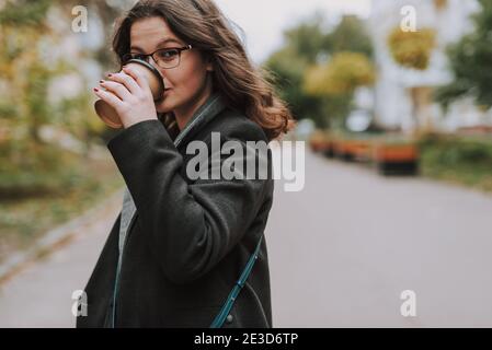 Attraktive junge Dame in der leeren Straße stehen allein und Suchen Sie ruhig, während Sie einen Schluck Kaffee trinken Eine Papiertasse Stockfoto