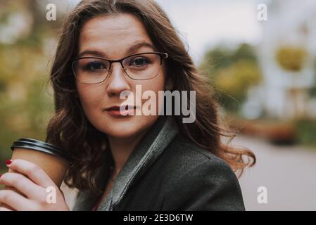 Porträt von attraktiven bebrilltacled junge Frau in der Straße halten Eine Tasse Kaffee zum Annehmen Stockfoto