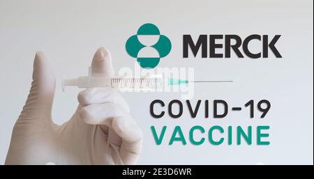 Hand mit Handschuh hält die Spritze neben dem Merck-Logo, einem der Unternehmen, das einen Covid-19-Impfstoff (Coronavirus) entwickelt. Wien, Österreich - 18. Januar 2021 Stockfoto