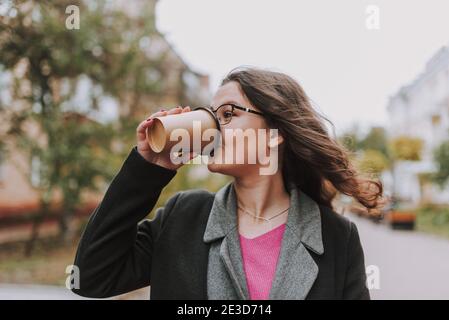Attraktive junge Frau trinkt Kaffee aus einem Pappbecher und Wegschauen Stockfoto
