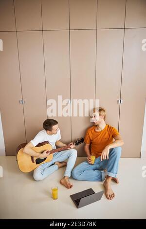 Hübscher junger Mann, der zu Hause Gitarre für seinen Freund spielt Stockfoto